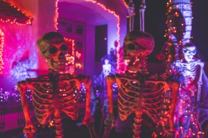 Two skeletons in front of halloween decorations lit by neon lights