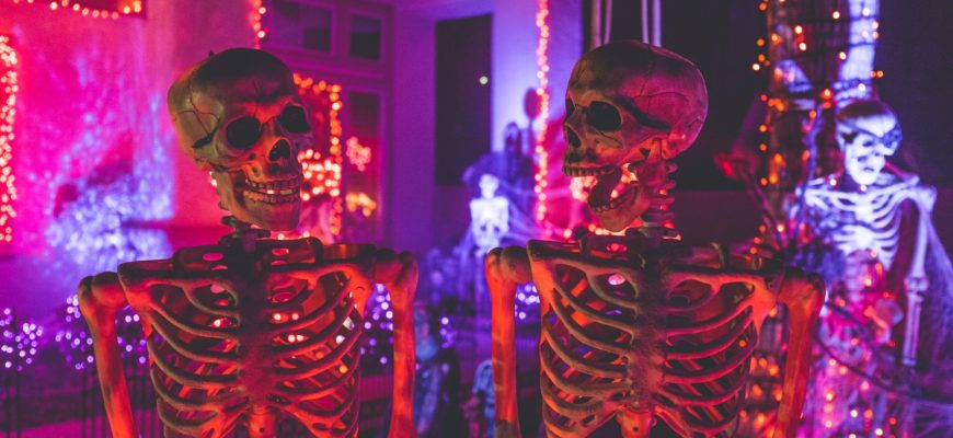 Two skeletons in front of halloween decorations lit by neon lights